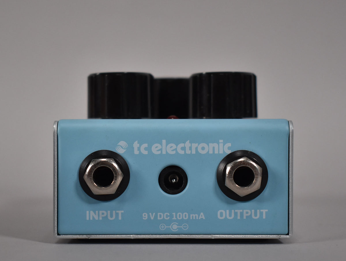 The light blue pedal's rear panel shows input and output jacks, a power input, and light wear on the silver metal casing.