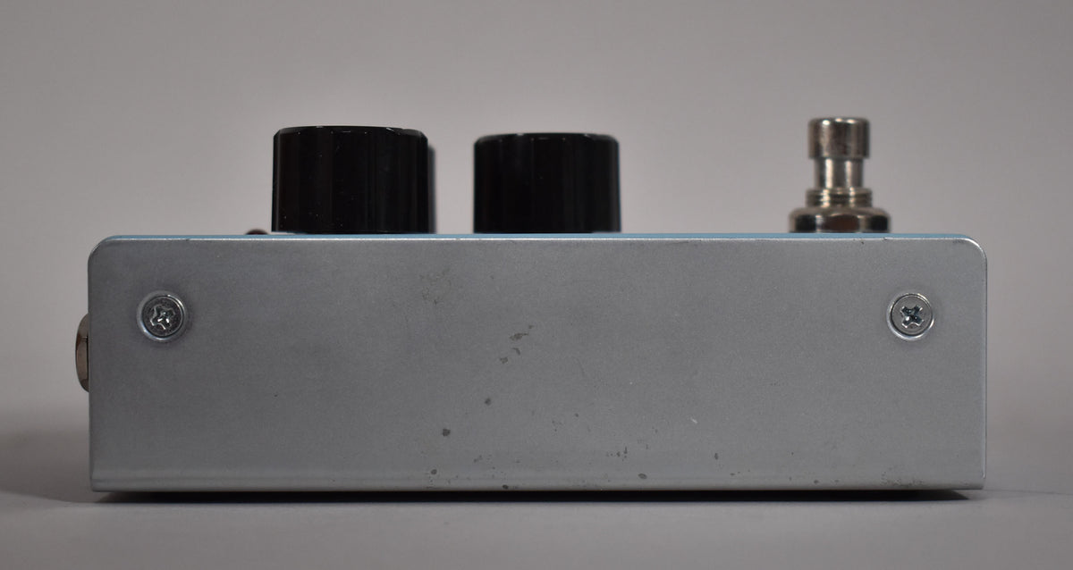 The reverb pedal is viewed from the side, revealing a light blue top, a silver side with minor scuffs, and two black control knobs.