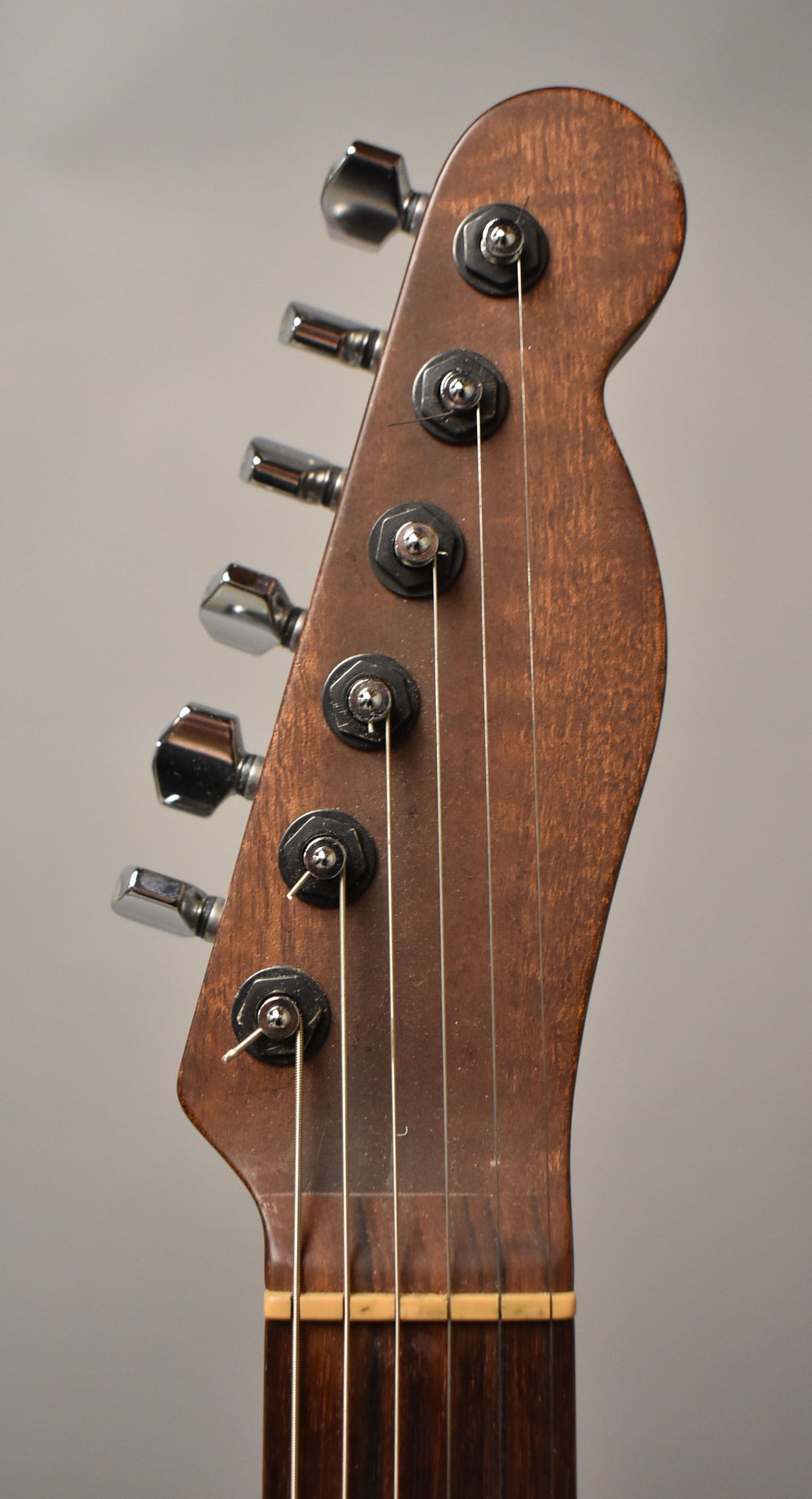 Close-up of the dark brown, natural finish headstock and upper fretboard, showing six chrome tuners and light strings.