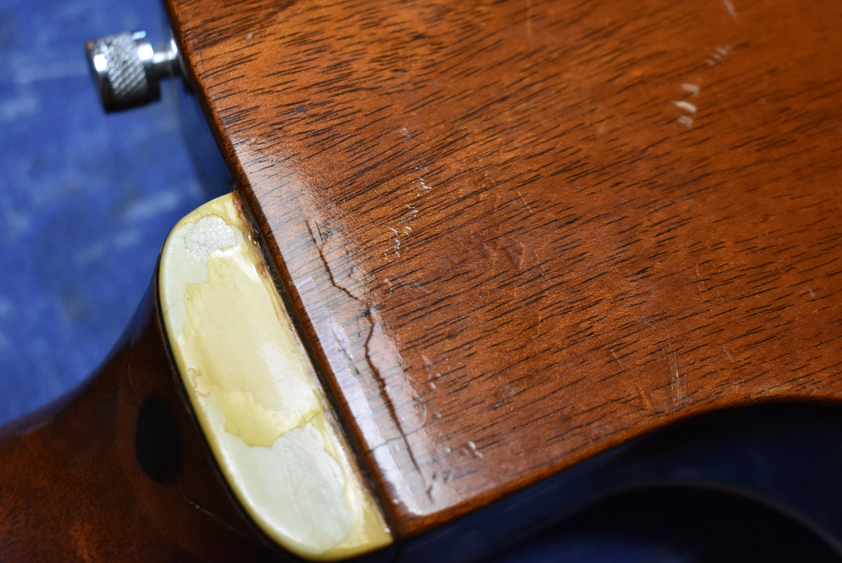 Close-up of the guitar's neck heel, showing finish checking, wear on the cream binding, and a visible crack in the wood.