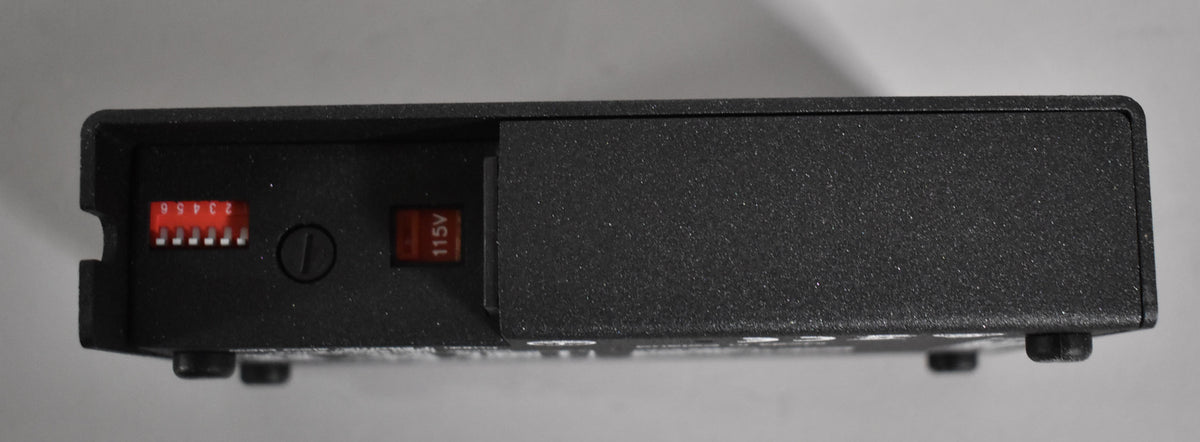 The black textured power supply is viewed from the side, revealing a red 6-position DIP switch and a red 115V voltage selector switch.
