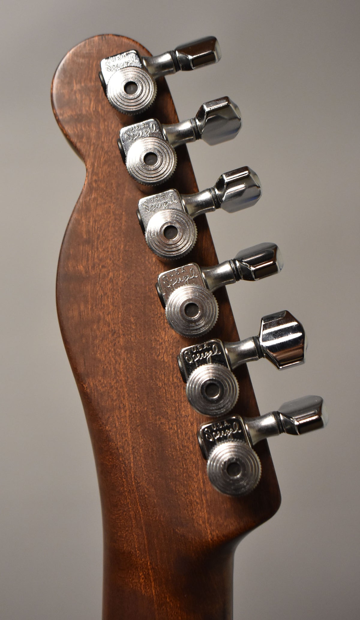 Close-up of the guitar's headstock, angled to the right, showing six chrome tuning pegs on a dark brown wood finish.