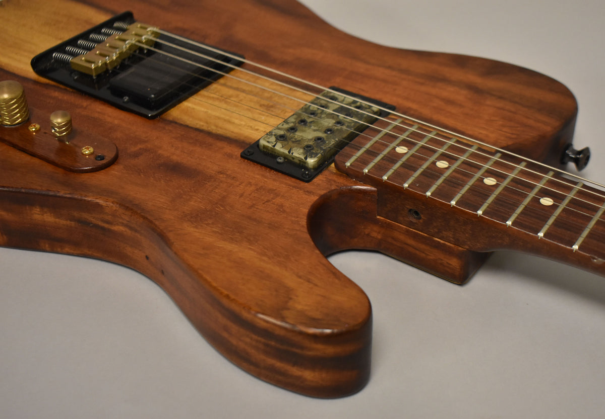 Close-up of a natural finish T-style guitar, showing the lower bout, bridge, pickups, and fretboard with dot inlays.