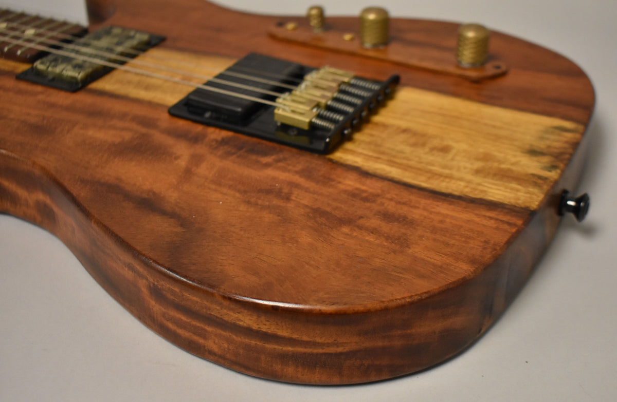 Close-up of the guitar's lower body, showing the natural wood grain, black bridge with brass saddles, and two brass control knobs.