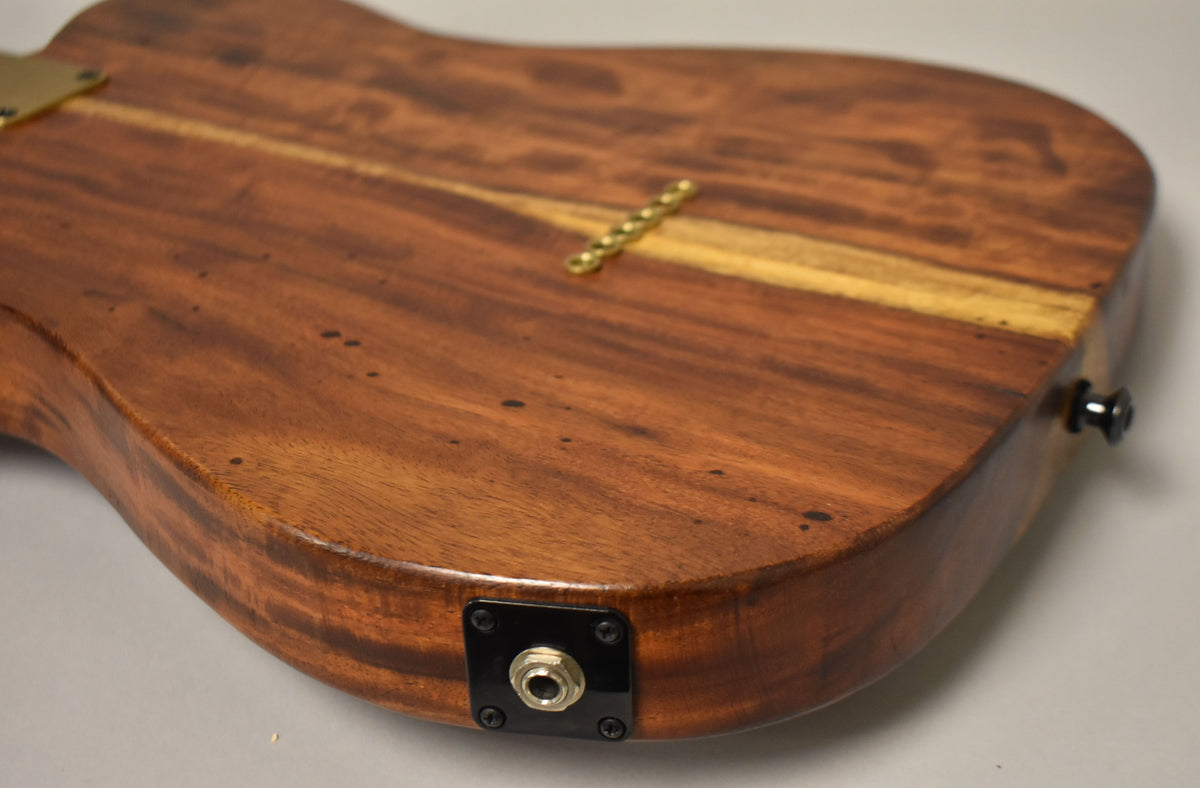 Close-up of the guitar's lower back, showing the natural wood grain, a black output jack plate, and a black strap button.