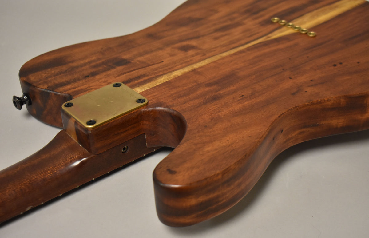 The guitar's natural wood back, with a lighter wood stripe, shows a brass neck plate and six brass string ferrules.