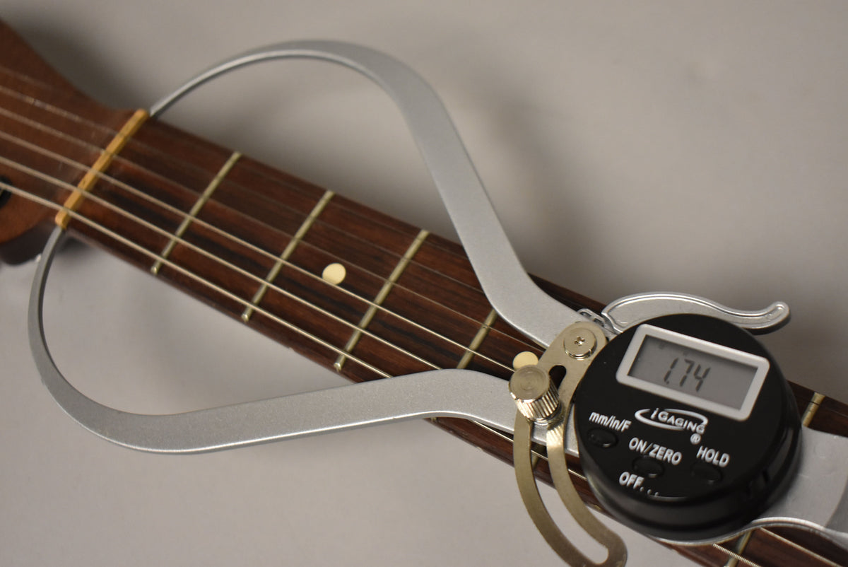 A digital caliper measures the guitar's dark rosewood fretboard at the nut, displaying 1.74 inches.