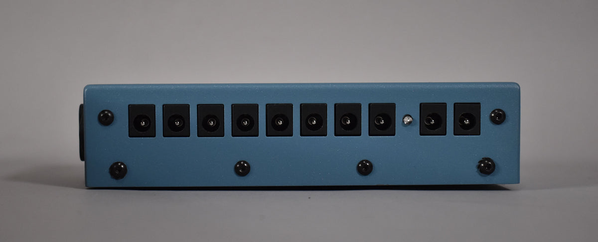 The blue power supply is viewed from the rear, showing ten black DC power outputs and a small silver toggle switch.