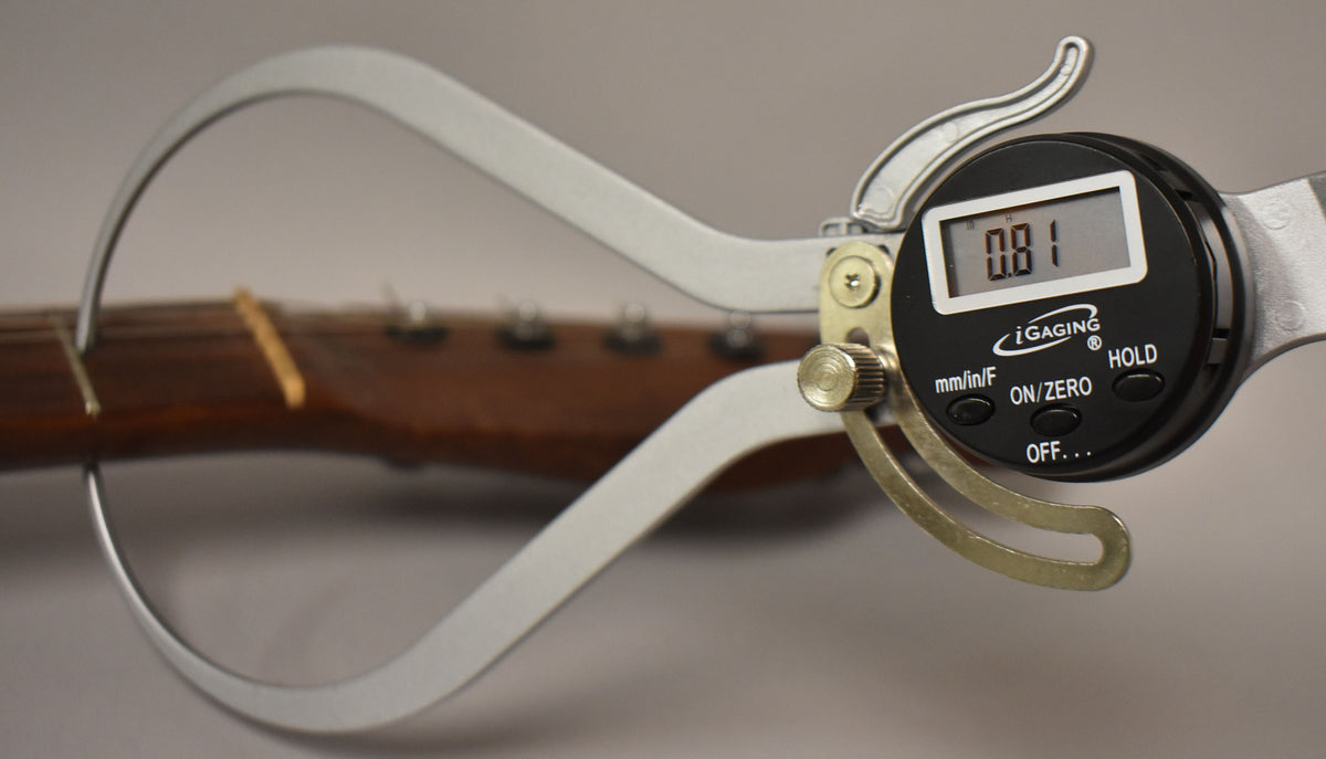 A digital caliper measures the nut width of the dark brown rosewood neck, showing 0.81 on its display.