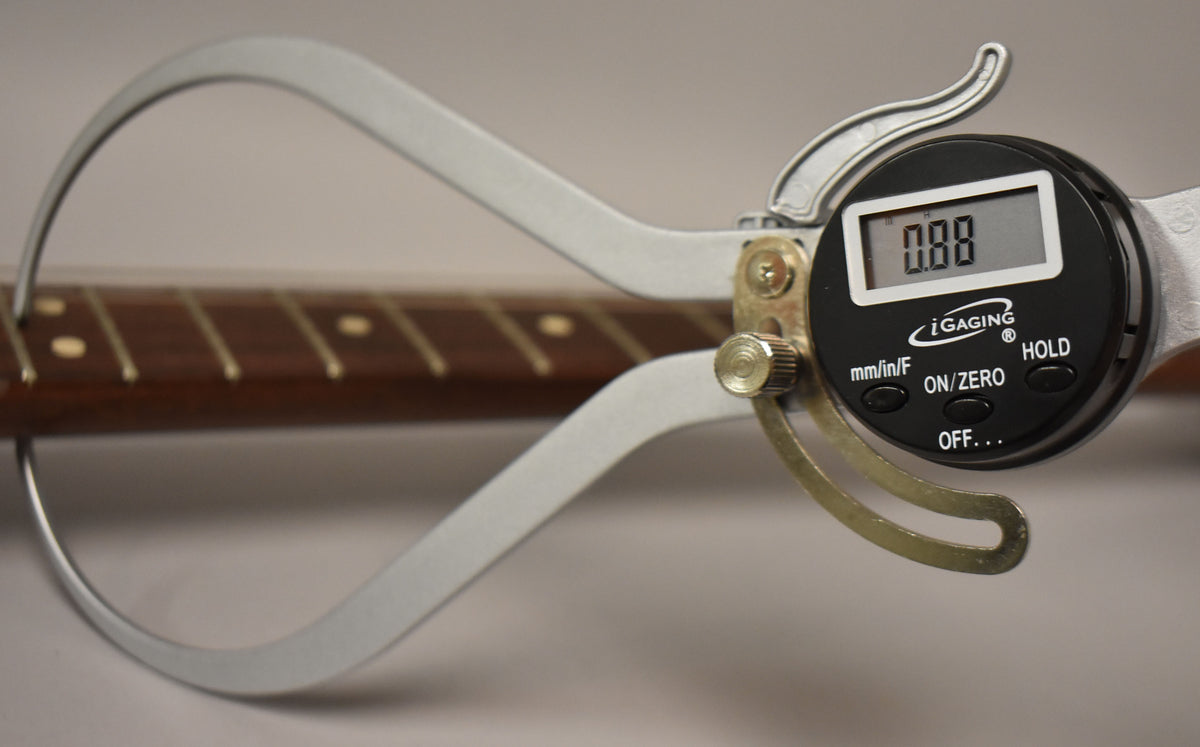 A digital caliper measures the dark brown rosewood fretboard with light dot inlays, displaying "0.88" on its screen.