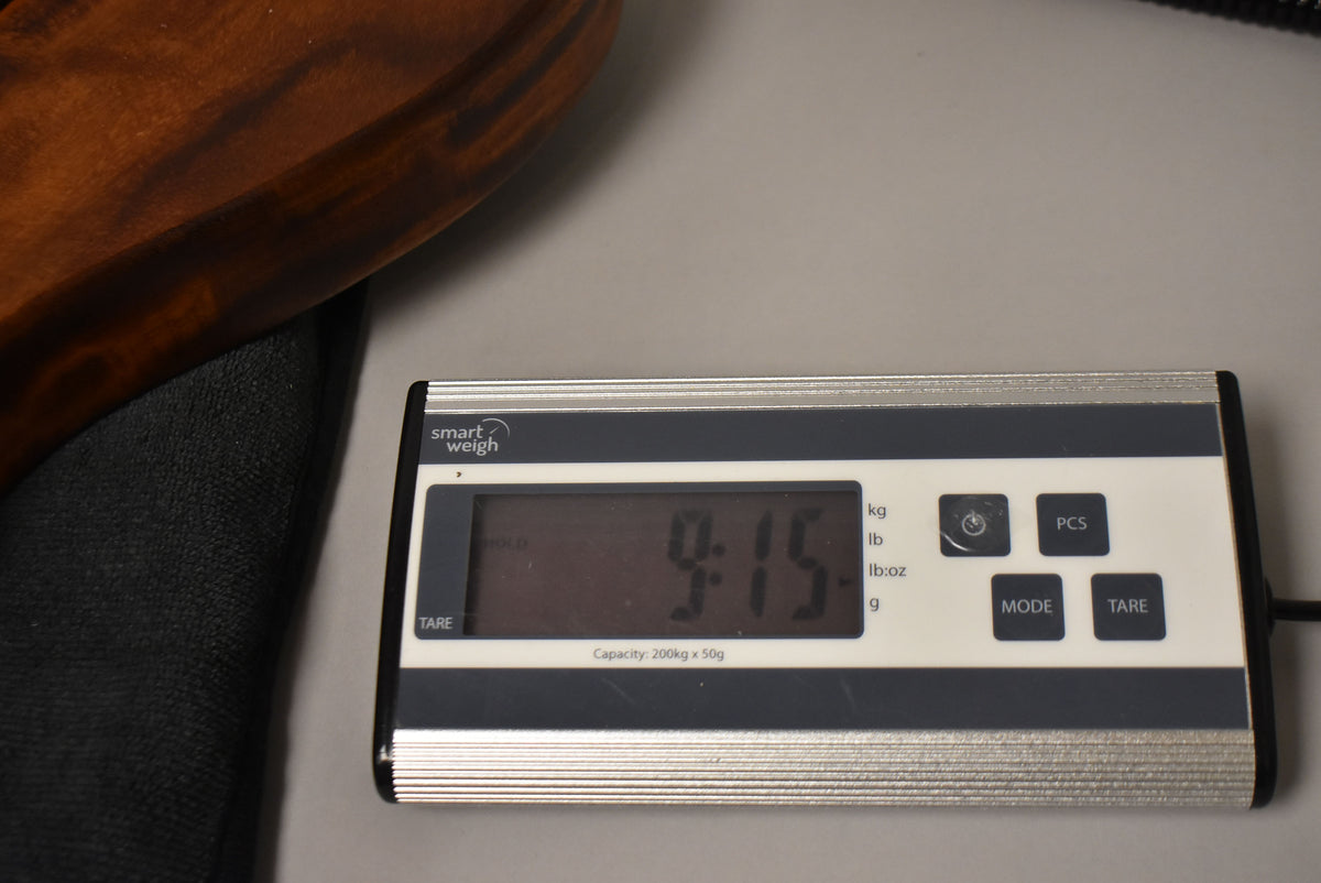 A close-up of a digital scale displaying "9.15" pounds, with a dark brown guitar body partially visible on the left.