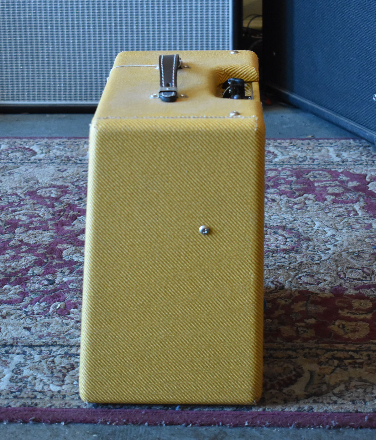 Right side of the lacquered tweed amp, showing the brown leather handle, a black input jack, and a single silver foot.
