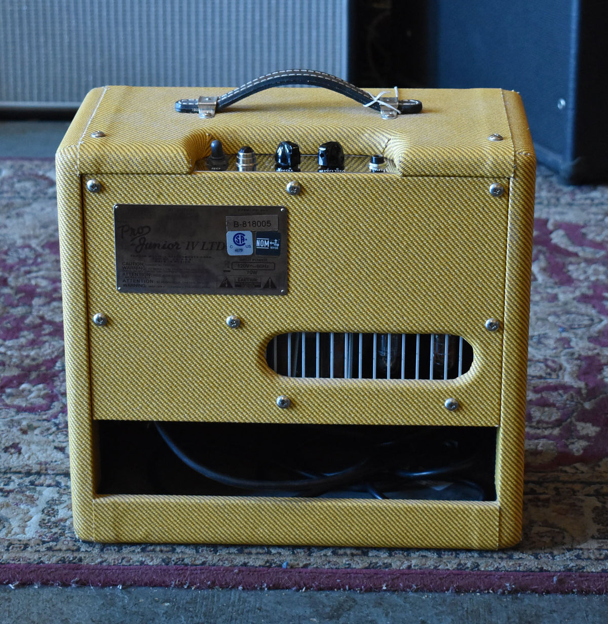 Rear view of a lacquered tweed combo amp, showing the control panel, a metal grille, and the power cable.