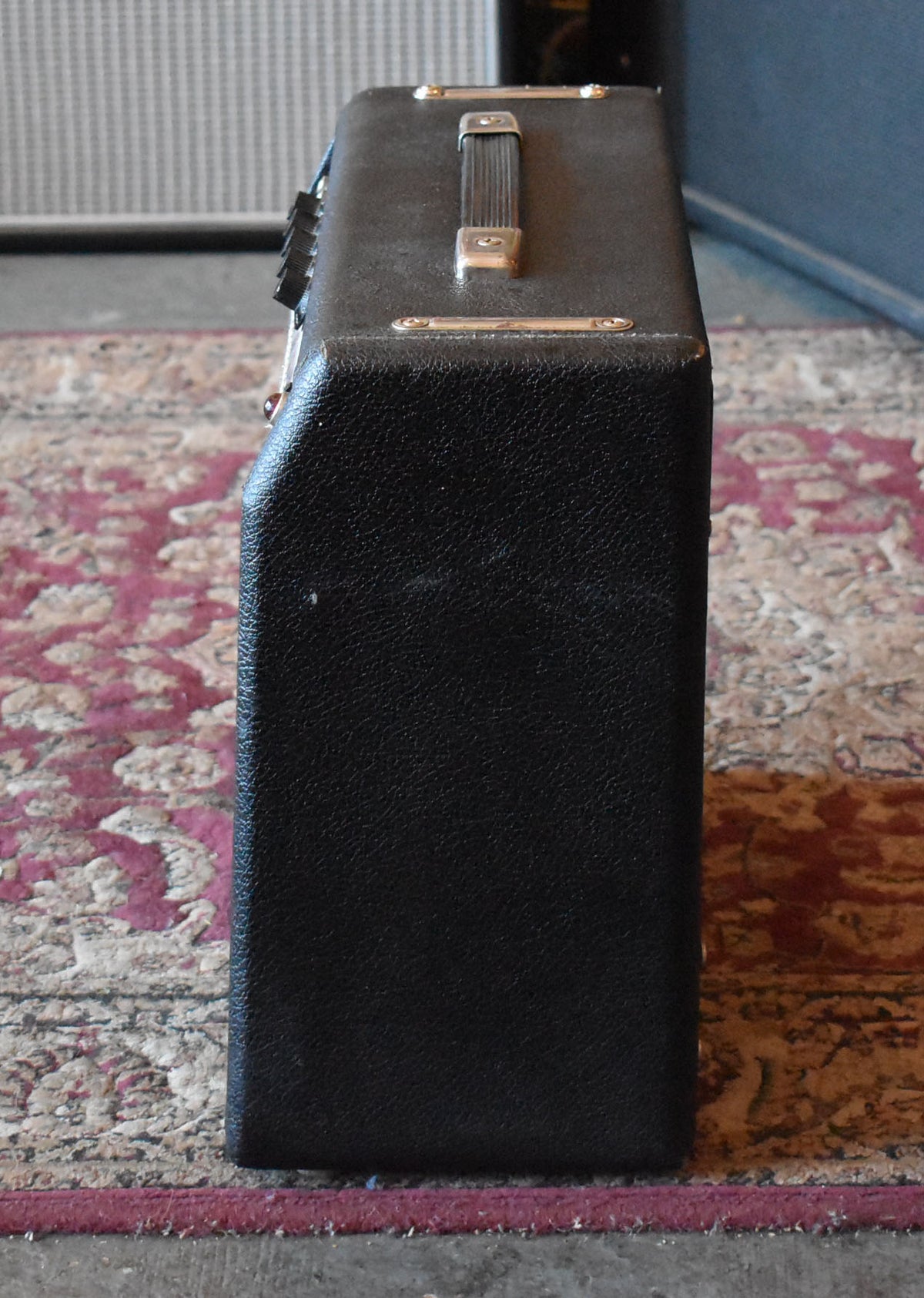 The black textured amp is viewed from the right side, showing a silver handle with gold-colored brackets on top and some wear on the tolex.