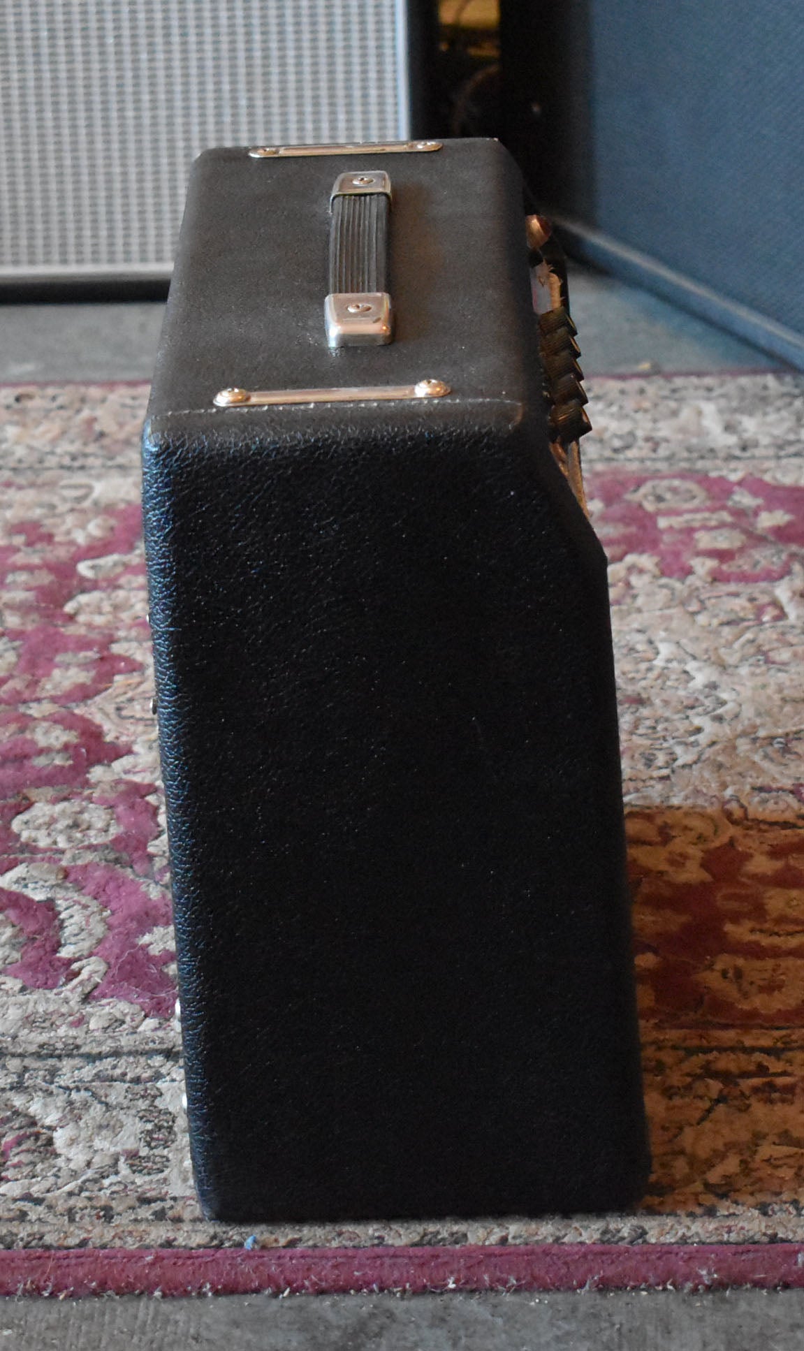 Side view of the black textured amp, showing the top handle, gold corner protectors, and a row of black knobs on the back.