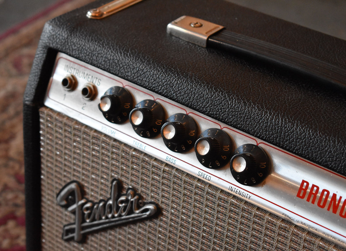 Angled close-up of a black tolex amp with a brown grille, silver control panel, black knobs, and a top handle.