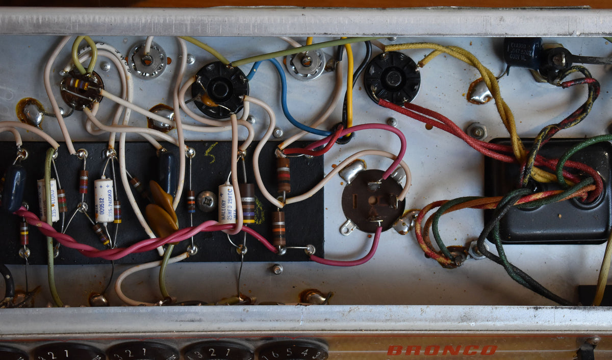 Overhead view of the amp's silver chassis, revealing colorful wiring, resistors, capacitors, and tube sockets, with some solder joints visible.