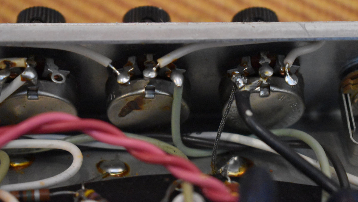 Close-up of the amp's internal wiring, showing three silver potentiometers with rust, connected by colorful wires and solder joints.
