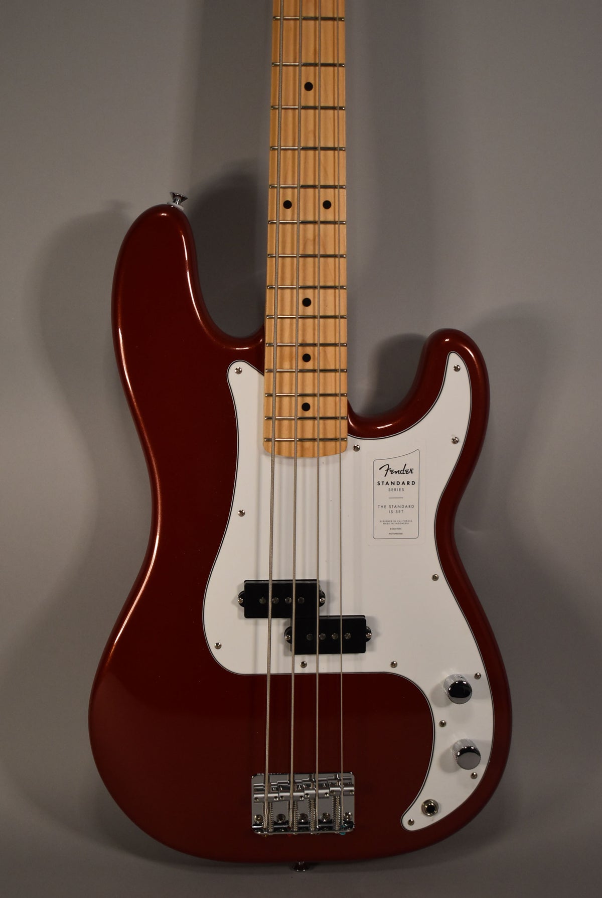 Full front view of a glossy candy cola bass guitar with a white pickguard, chrome hardware, and a maple fretboard.