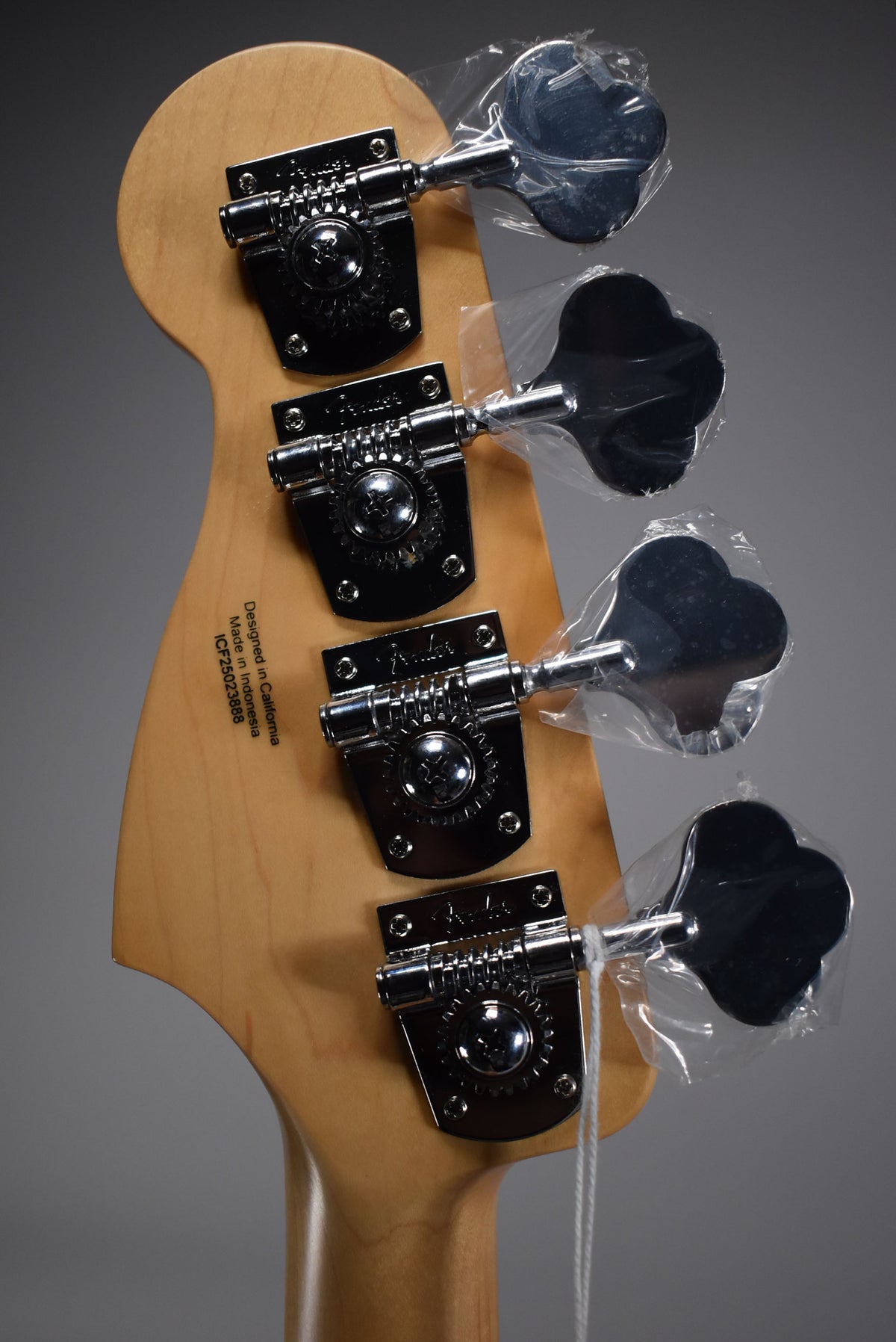 Rear view of the bass headstock, showing four chrome tuners with cloverleaf keys, still wrapped in clear plastic.