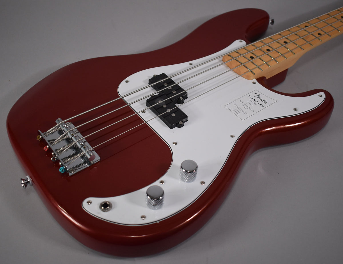Candy Cola Precision Bass, angled from above, showing the metallic red body, white pickguard, chrome bridge, and two control knobs.
