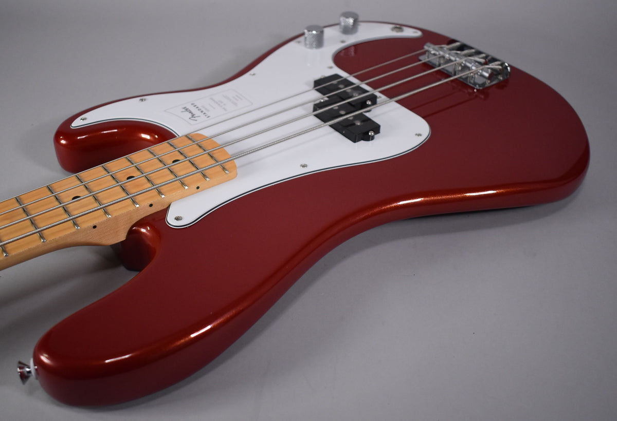 The Candy Cola bass body, with a white pickguard and maple neck, is angled from the lower left, showing the bridge and controls.