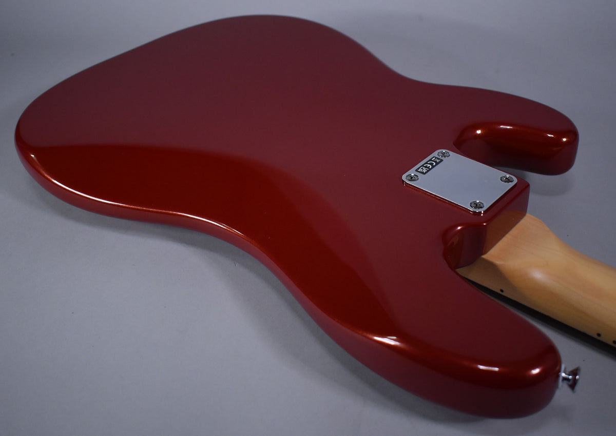The bass guitar's Candy Cola body, with a metallic sheen, is viewed from the back, showing the neck plate and strap button.