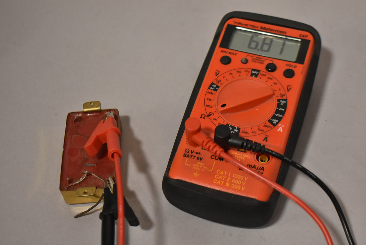 The pickup's gold-plated baseplate and red-brown underside are visible, with alligator clips attached to the wiring, next to a multimeter reading "6.81".