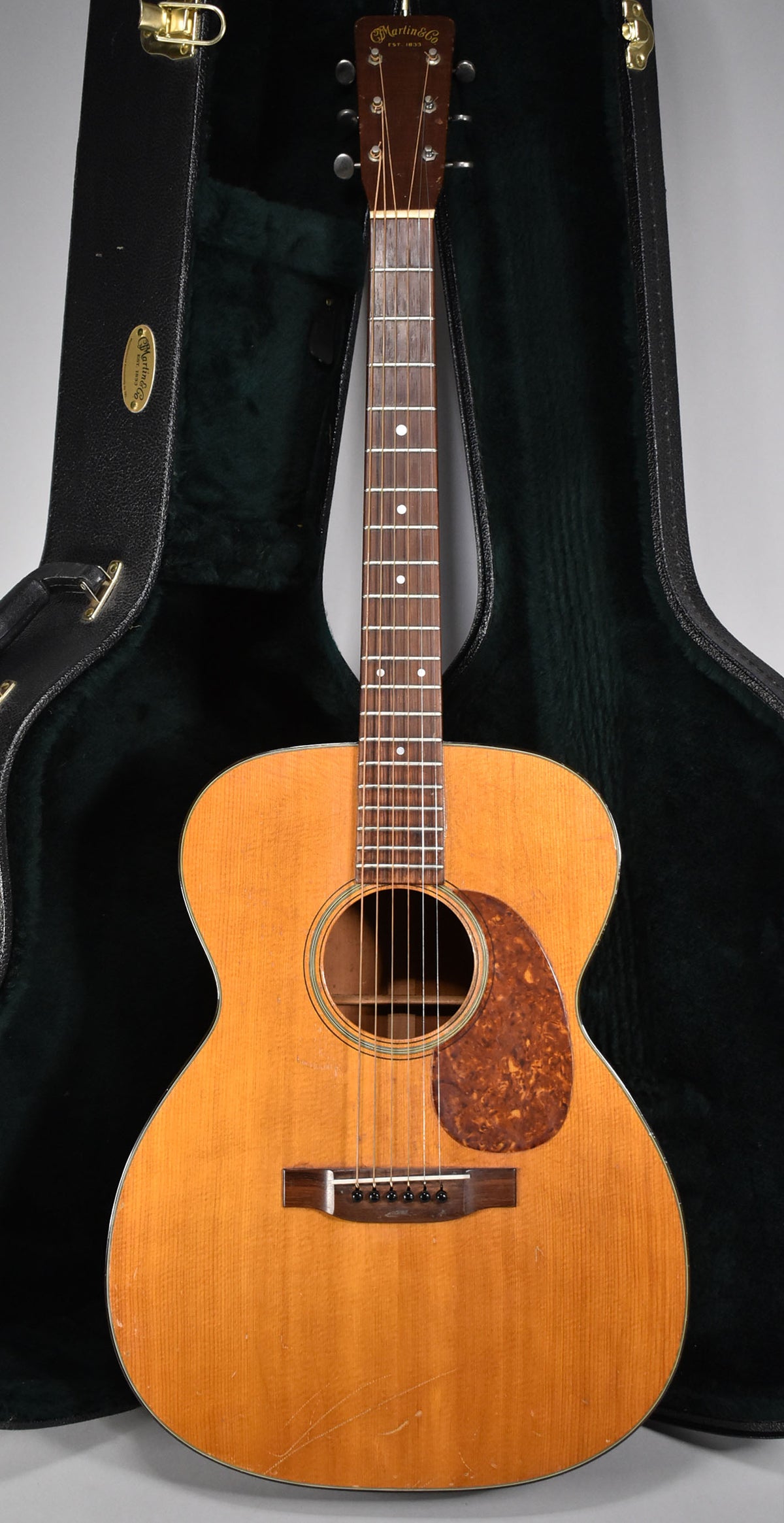Full-front view of a natural finish acoustic guitar with a dark tortoiseshell pickguard, showing visible scratches and wear on the body.