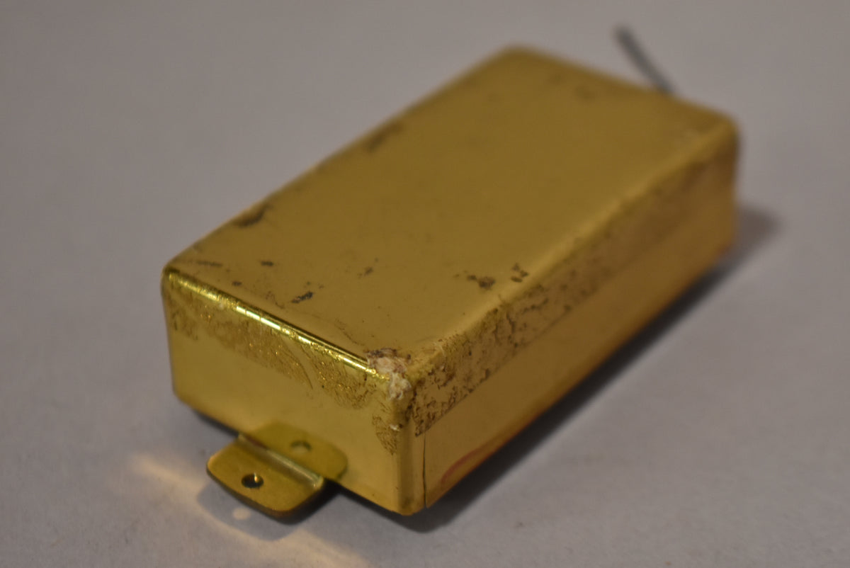 The gold humbucker pickup is angled, showing its top and side, with heavy corrosion and wear on the edges and a mounting tab visible.