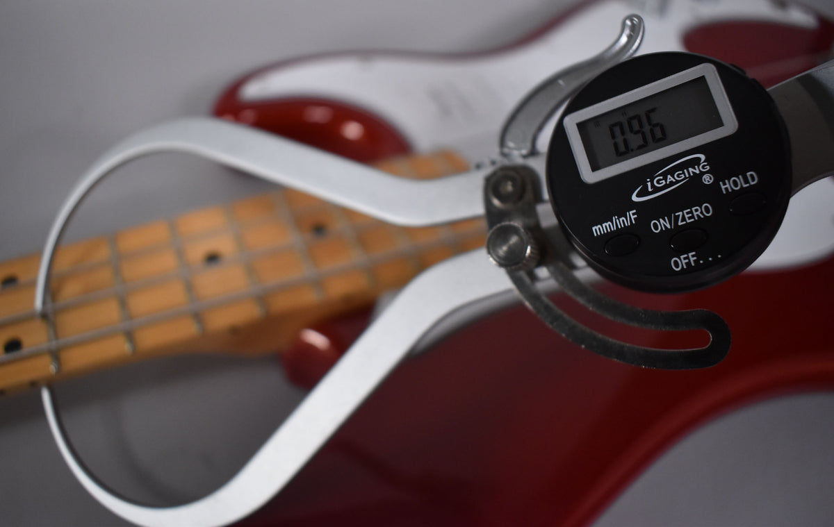 A digital caliper measures the Candy Cola bass's fret height at 0.96, with its maple fretboard visible.