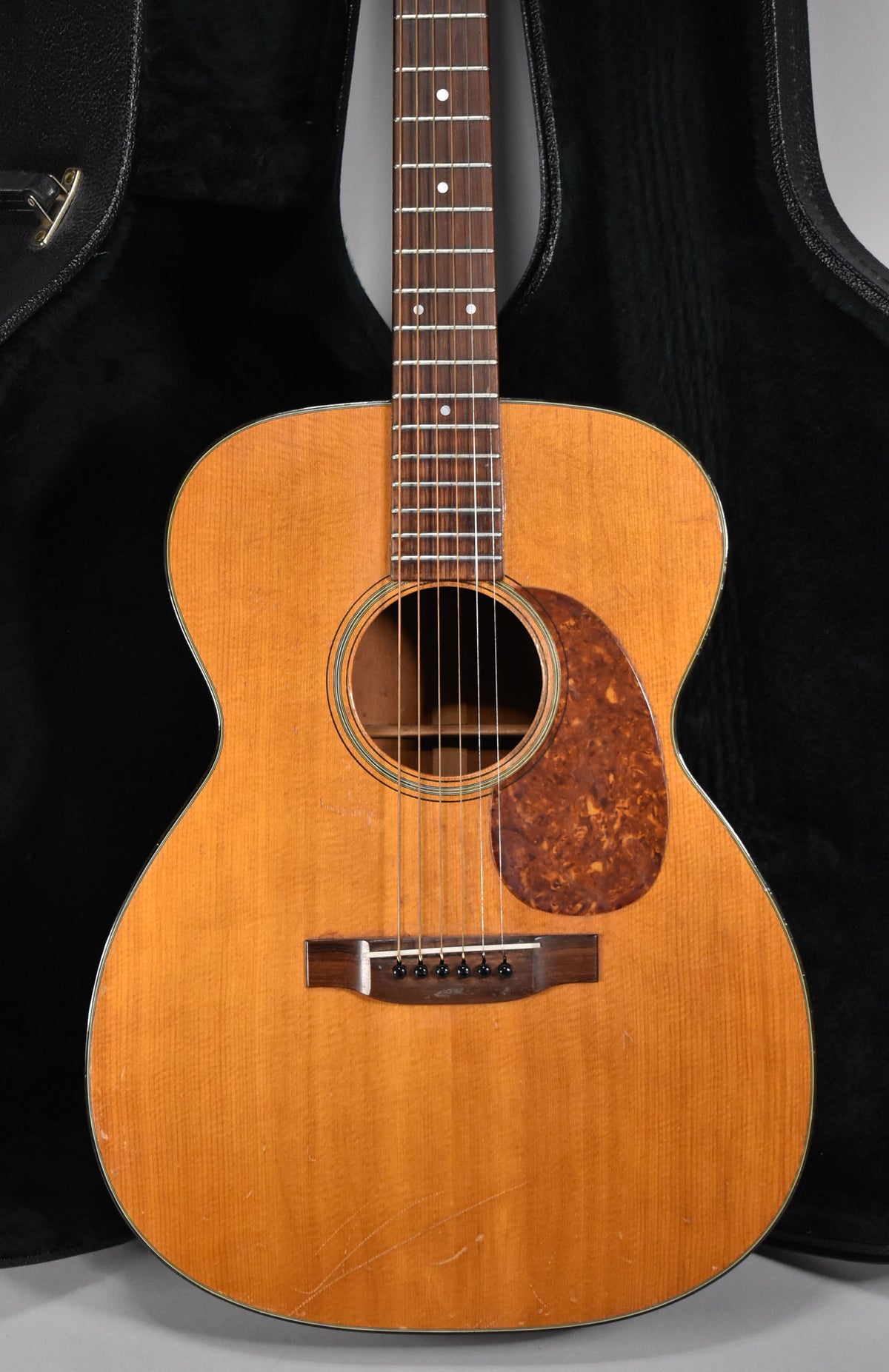 Full-frame view of the natural finish acoustic guitar, showing the body, pickguard, bridge, and lower fretboard with wear.