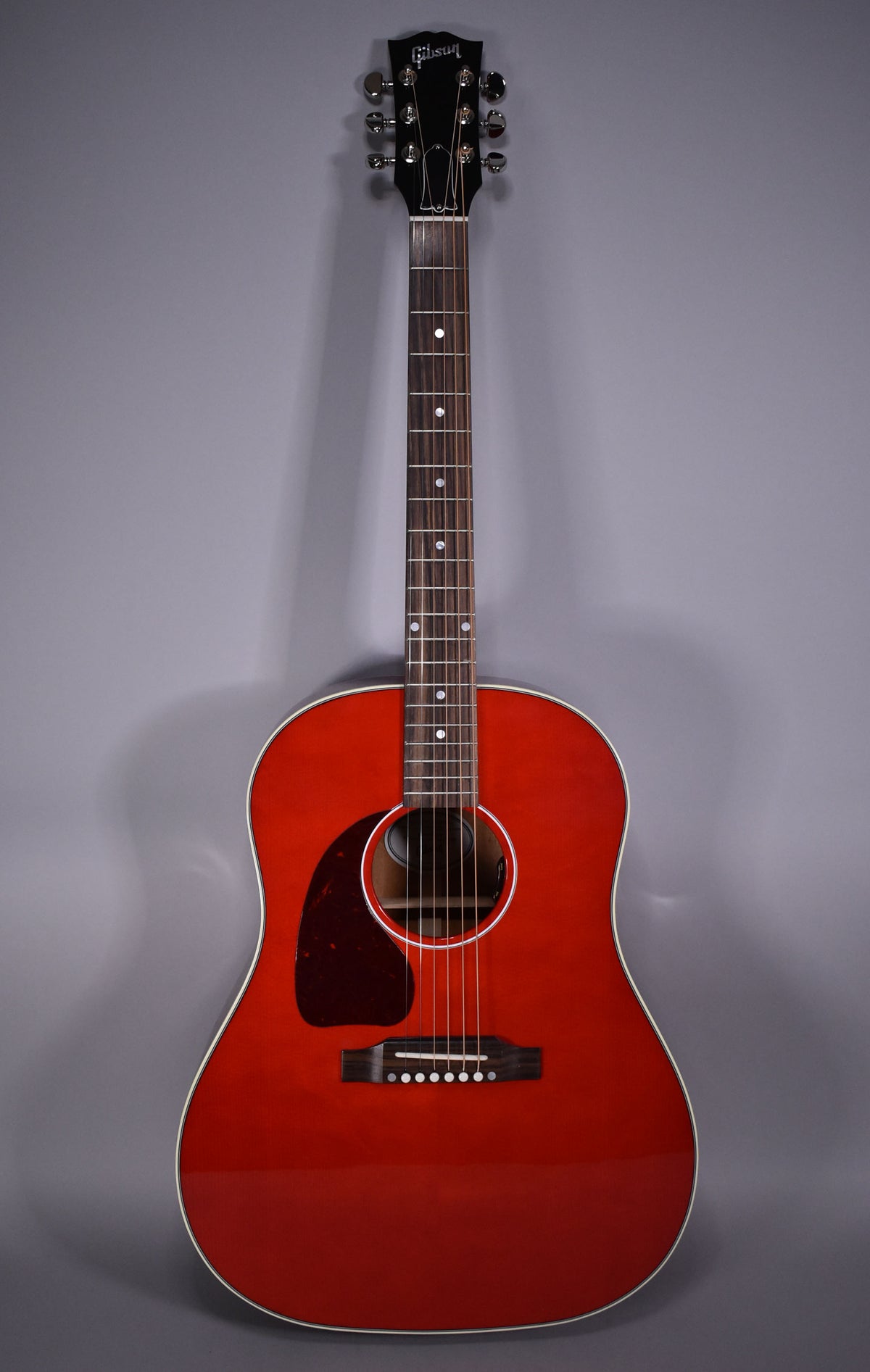 Full front view of a cherry red acoustic guitar with a dark pickguard, white binding, and chrome tuners.