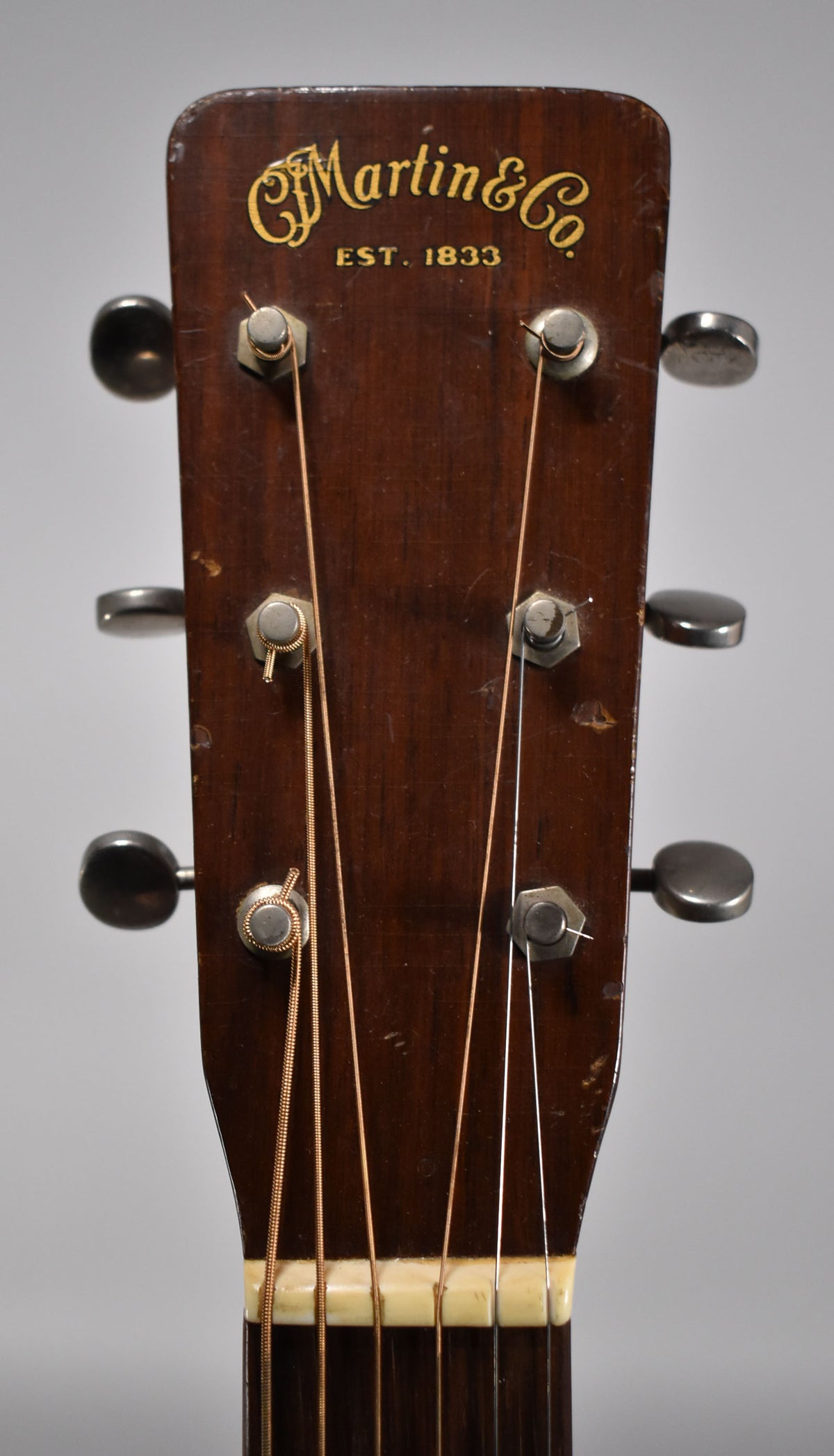 Close-up of the dark brown headstock, showing six metal tuners, a cream nut, and light wear on the dark finish.
