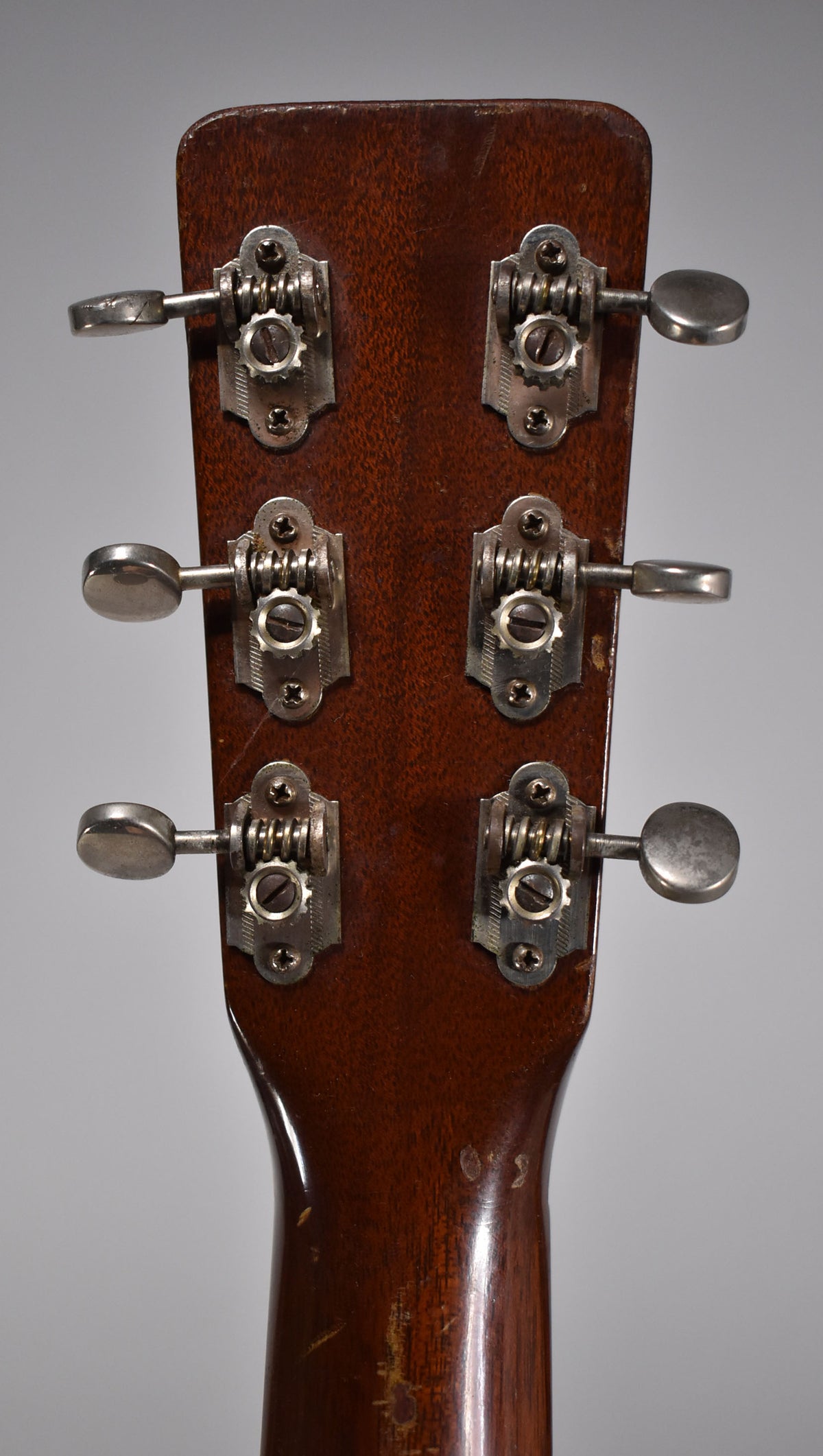 The guitar's dark brown headstock and neck are viewed from behind, showing six tarnished silver tuners and finish wear.
