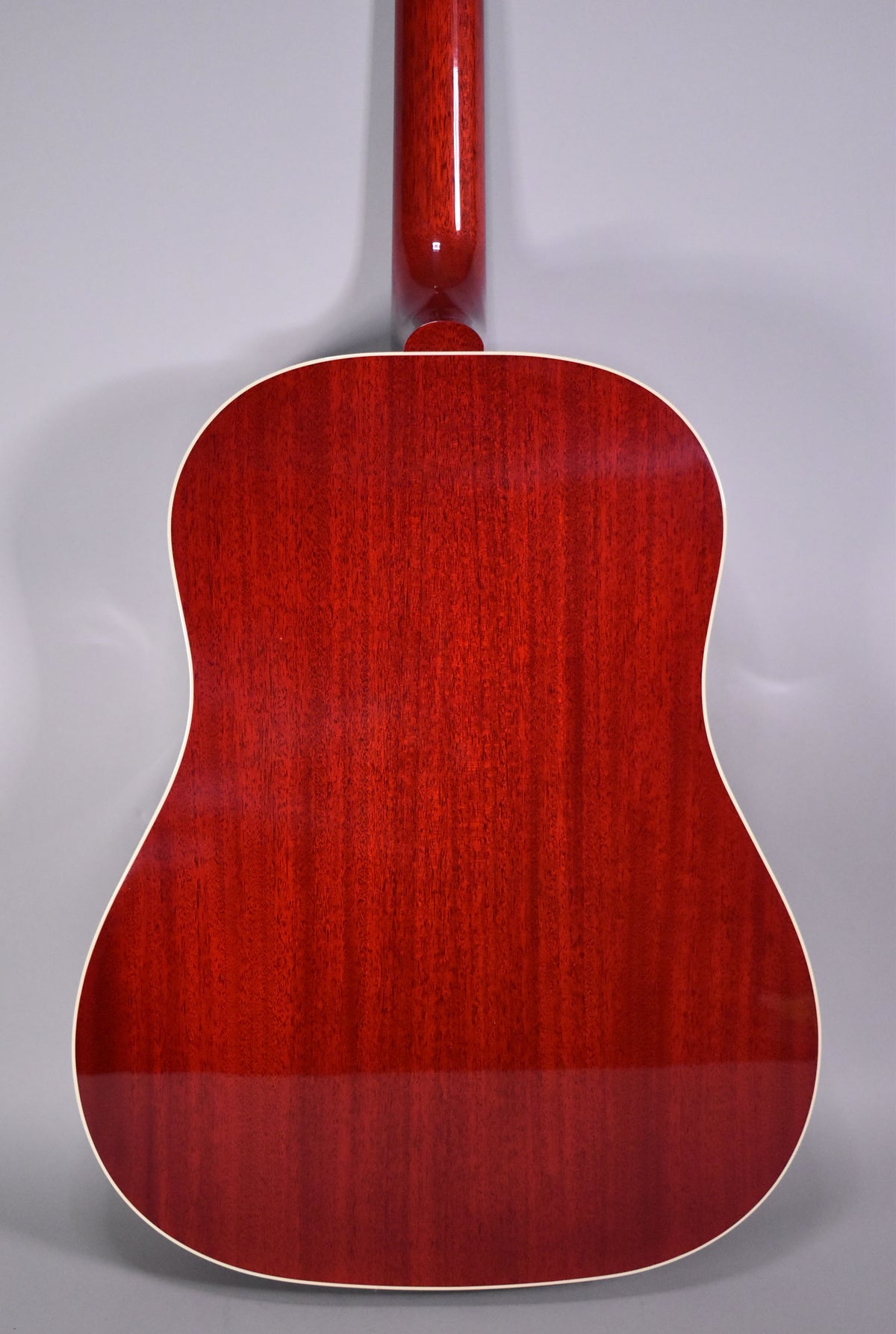 The full back of the cherry-finished acoustic guitar is visible, showing the wood grain and cream binding along the edges.