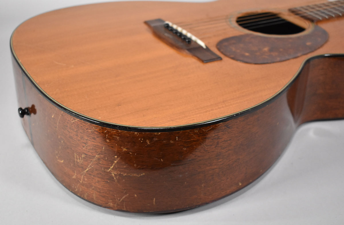 The lower bout of a natural finish acoustic guitar, showing a dark brown pickguard, bridge, and heavy finish wear on the side.