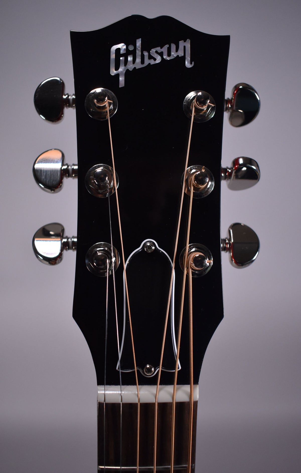 Close-up of a black headstock with six chrome tuners, a white truss rod cover, and light-colored strings.