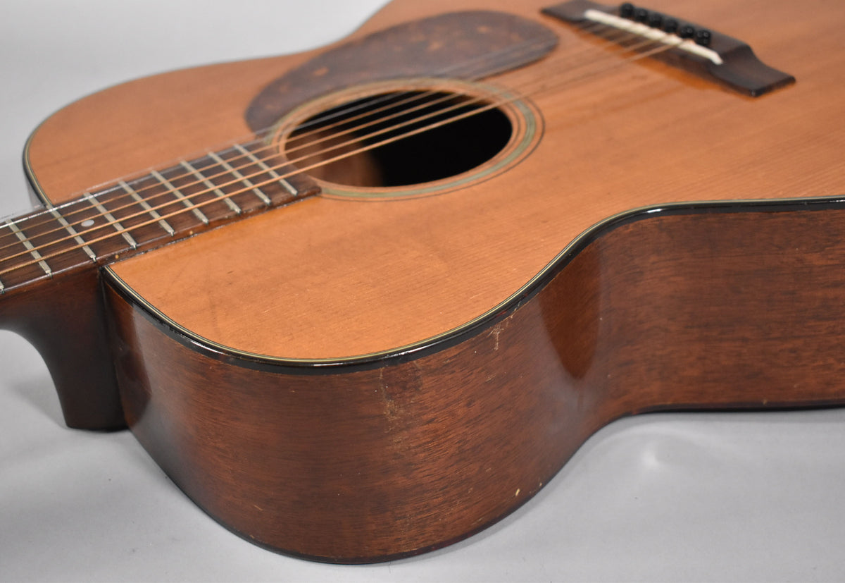 The acoustic guitar's lower bout and waist are framed, showing a natural finish with visible wear and checking on the dark wood sides.