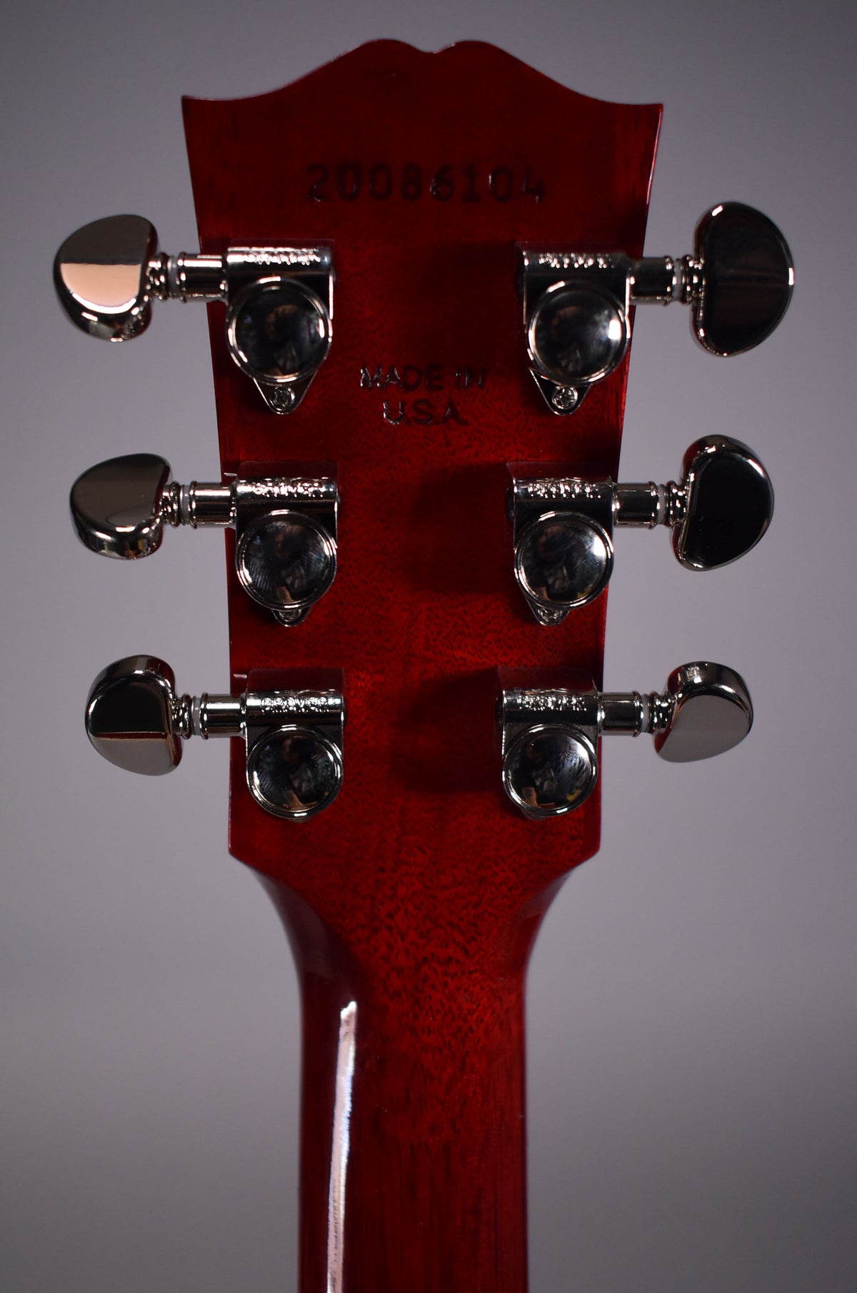 The back of a cherry red headstock and neck, showing six chrome tuners with kidney bean buttons.