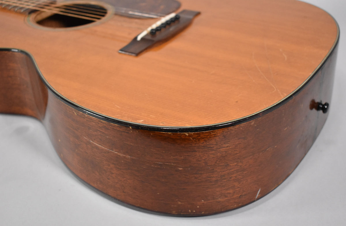 Close-up of the lower bout of a natural finish acoustic guitar, showing heavy wear, scratches, and checking on the body and sides.