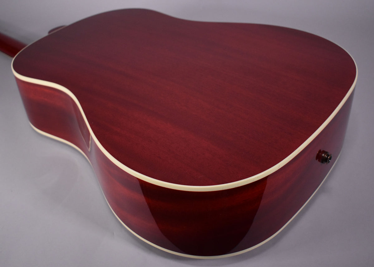 The back of a cherry-finished acoustic guitar, showing the grain, cream binding, and a dark endpin jack on the lower bout.