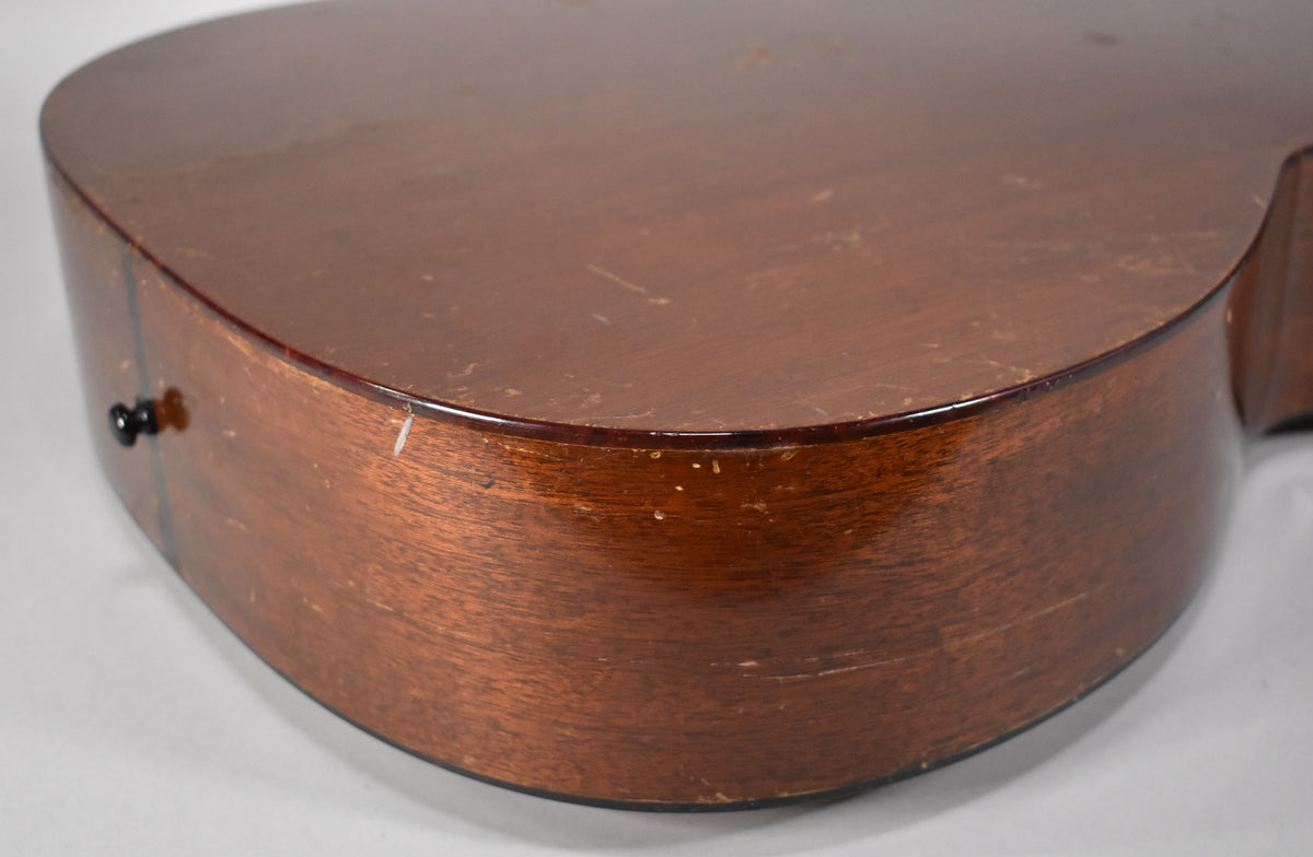 The lower bout of a dark brown acoustic guitar, showing a black endpin, scuffs, and finish wear on the sides and back.