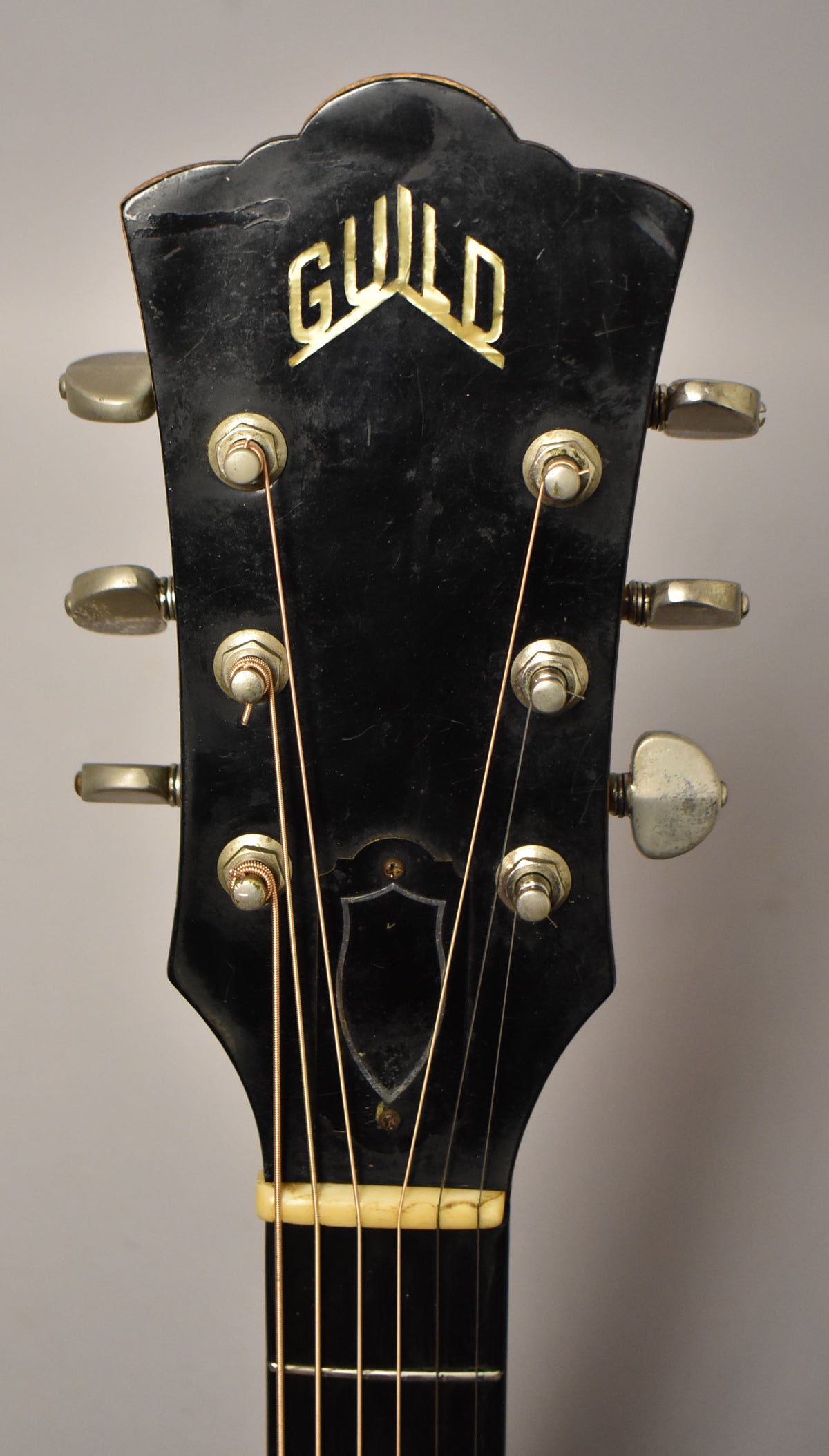 Close-up of the guitar's black headstock with six tarnished tuners, showing finish wear and a chipped nut.