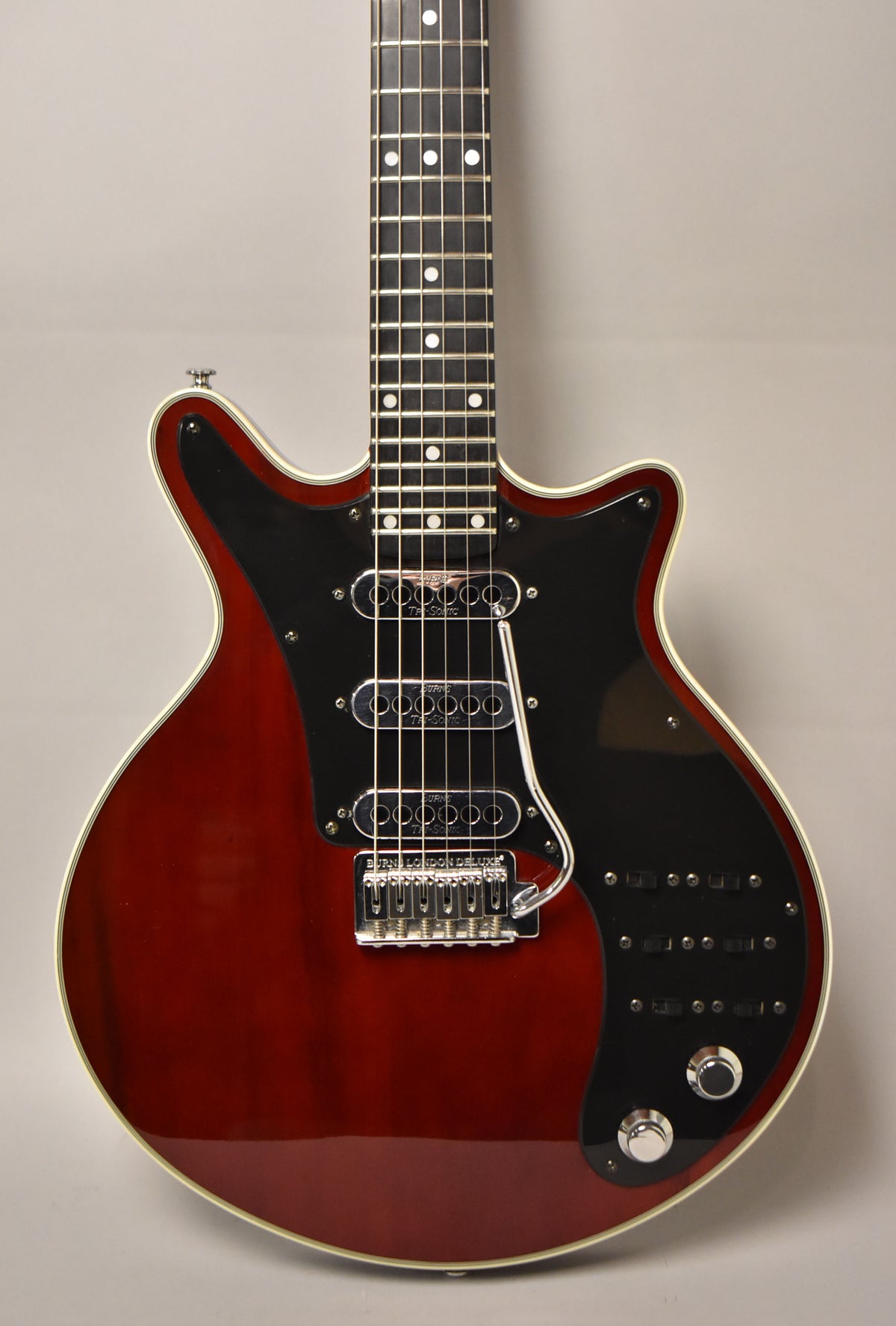 The cherry red guitar, angled slightly right, features a black pickguard, three chrome pickups, and six black slider switches.