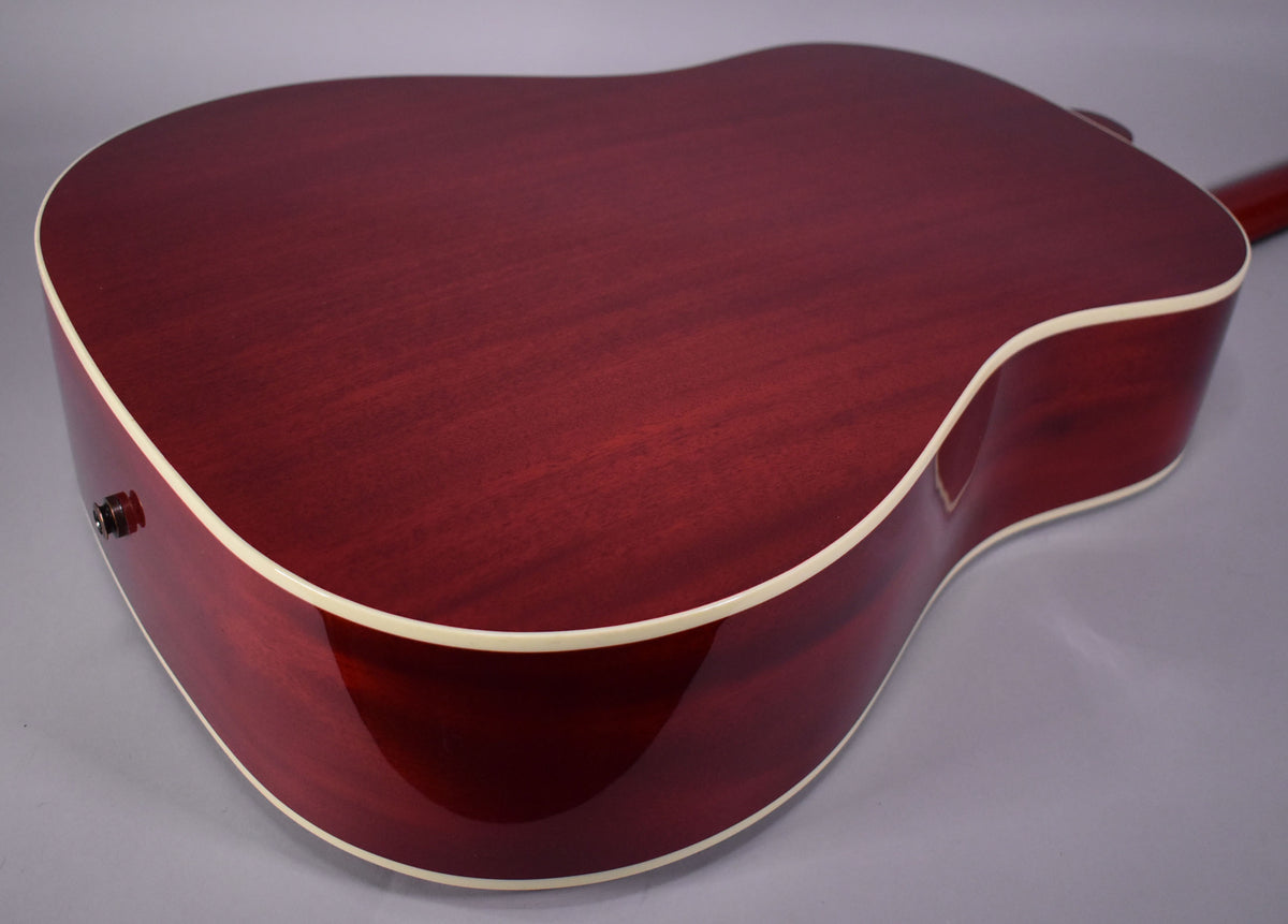 The back of a cherry-finished acoustic guitar with visible wood grain and cream binding, angled from the lower bout to the upper.