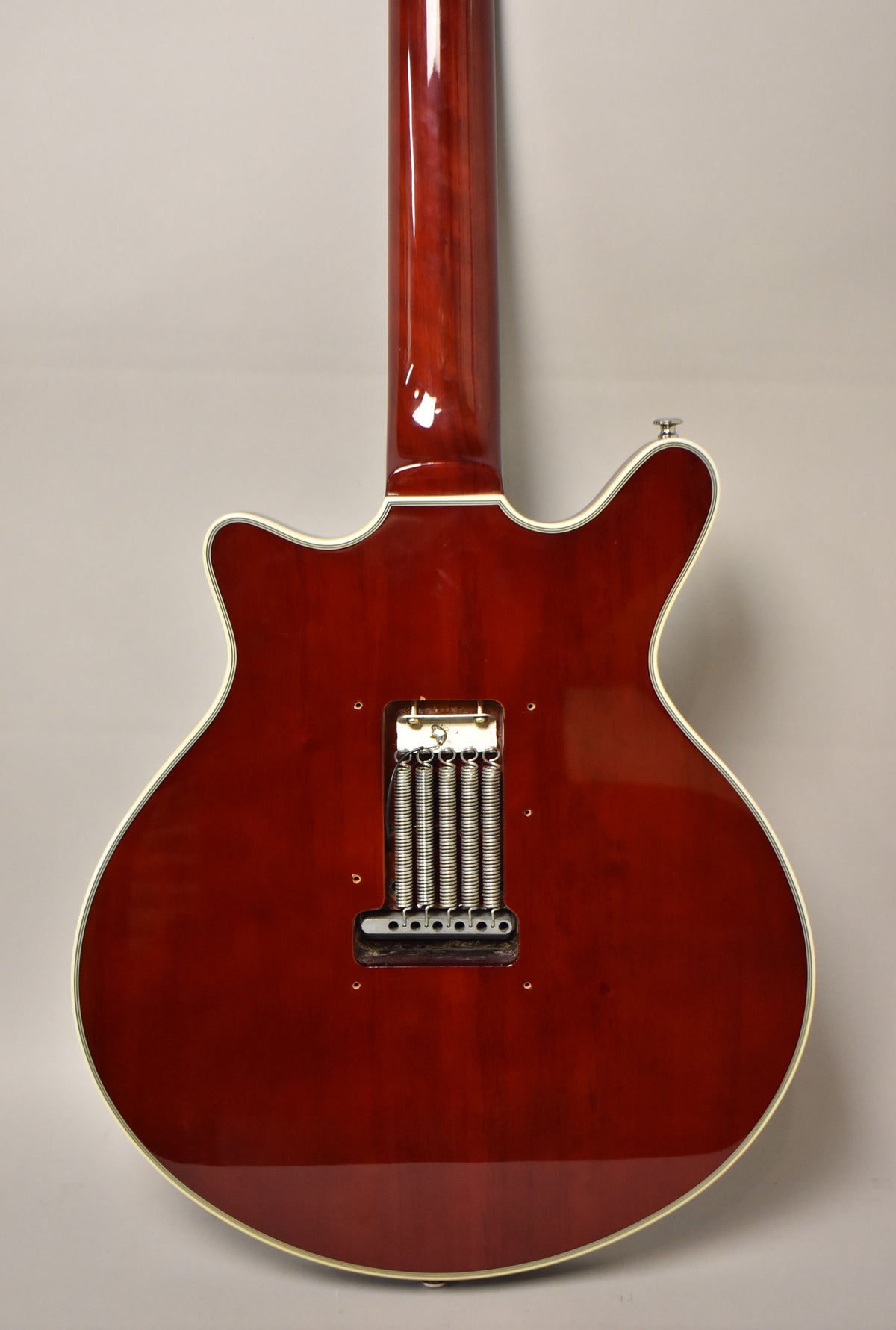 Rear view of a cherry red guitar with a glossy finish, showing the neck joint and the tremolo spring cavity with five springs.
