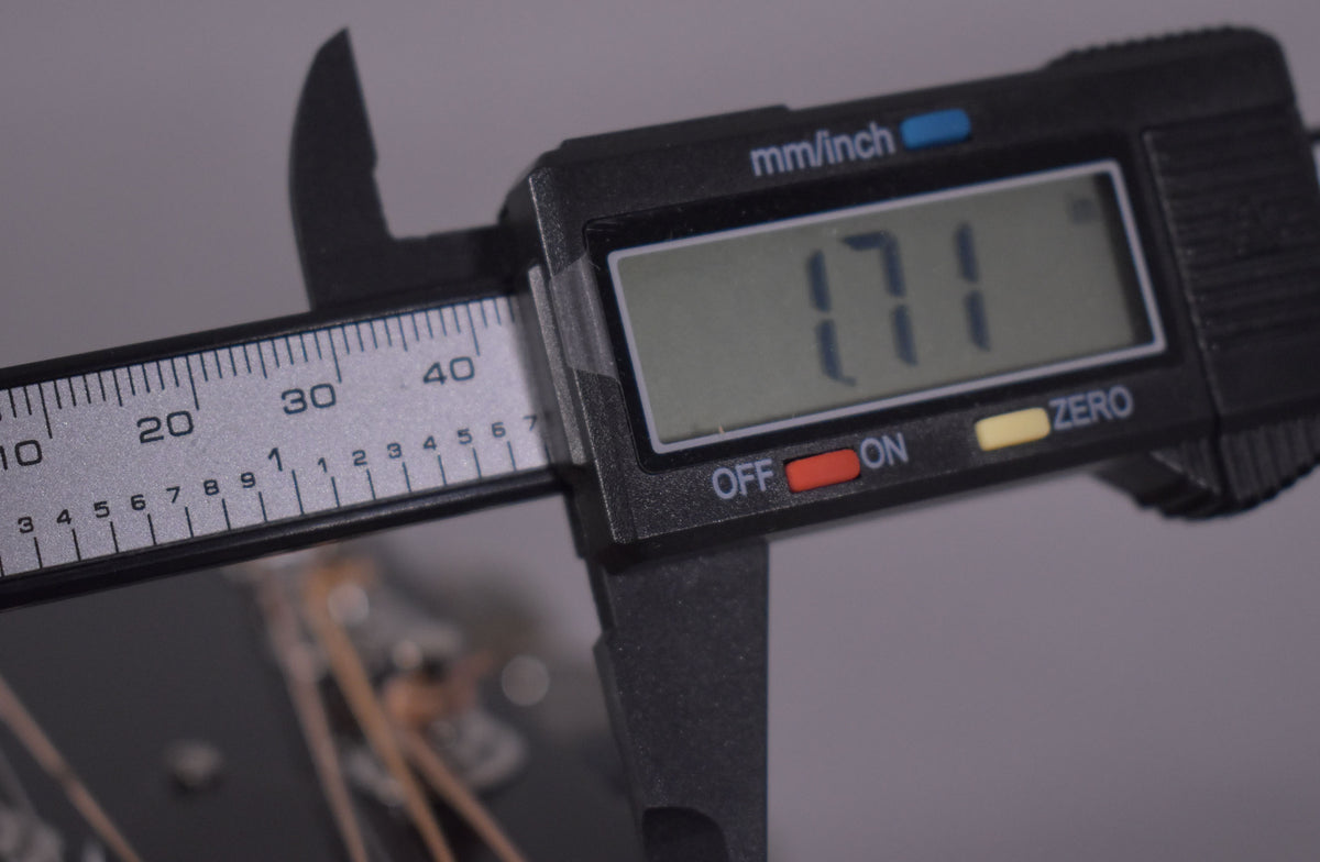 A digital caliper measures the nut width of the guitar, displaying "1.71" inches, with strings visible below.