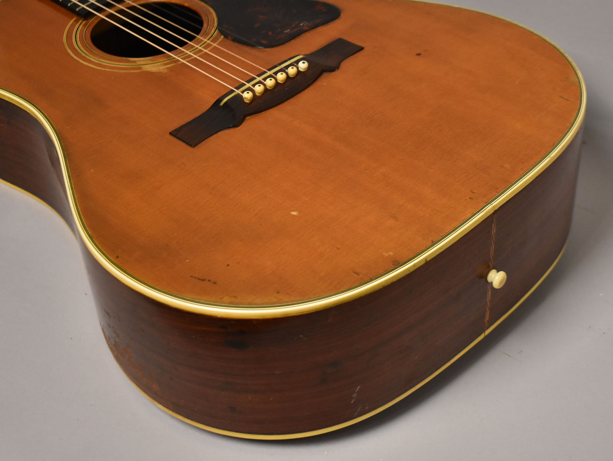 Upper body of a natural acoustic guitar, showing the soundhole, bridge, pickguard, and dark sides with a cream binding.