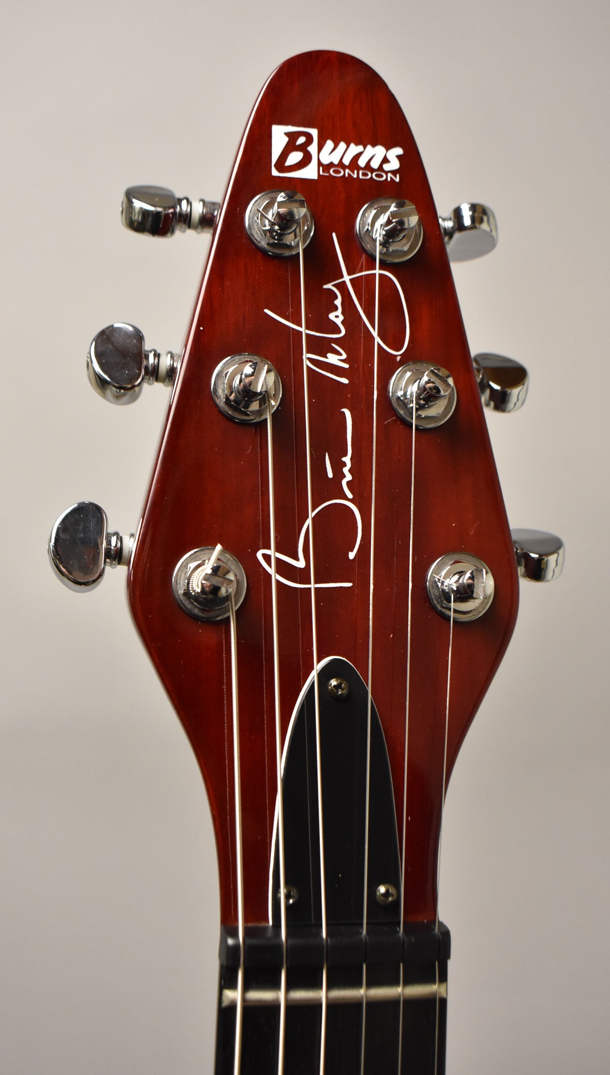 Close-up of the cherry red headstock with six chrome tuners, a black truss rod cover, and white signature.